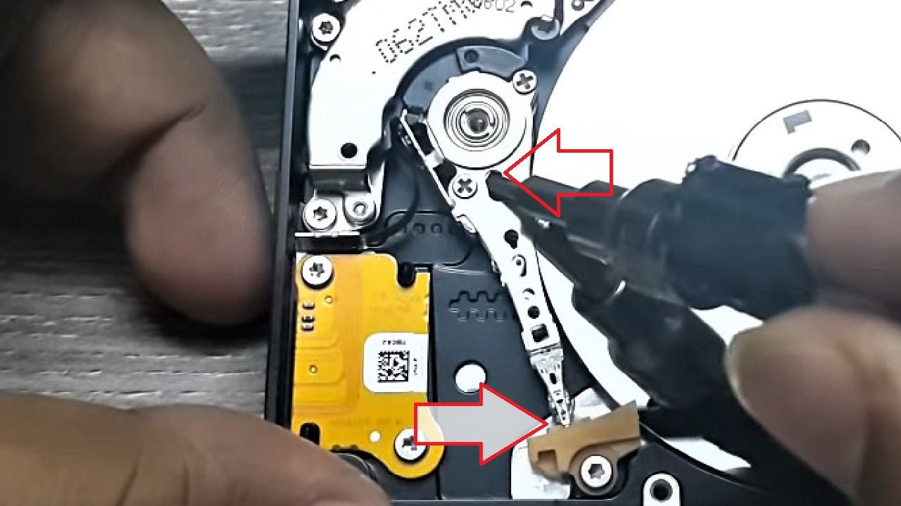 Holding the screwdriver in the hole on the arm of the disk head